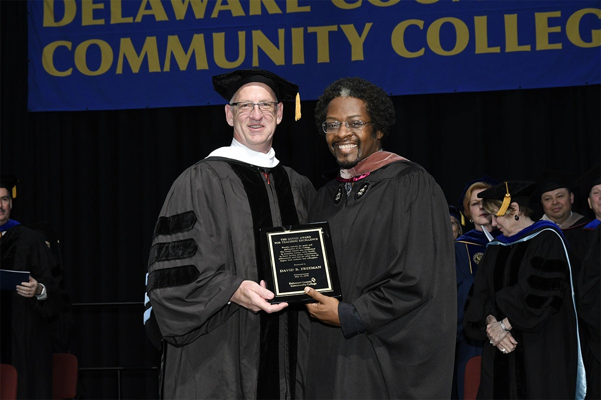 Associate Professor of English Dr. David Freeman (right) receives the 2018 Gould Award for Excellence in Teaching from Michael Ranck, chairman of the Board of Trustees of Delaware County Community College, at the College’s 2018 Commencement ceremony which was held at West Chester University.
